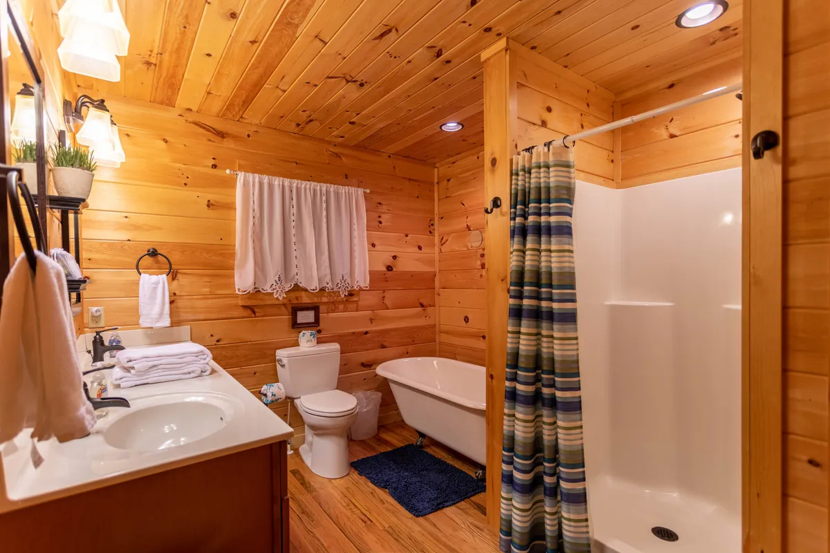 A tranquil bathroom scene with a rustic wooden vanity, a bathtub perfect for soaking, and a striped shower curtain. The wooden walls and ceiling enhance the warm, relaxing atmosphere.
