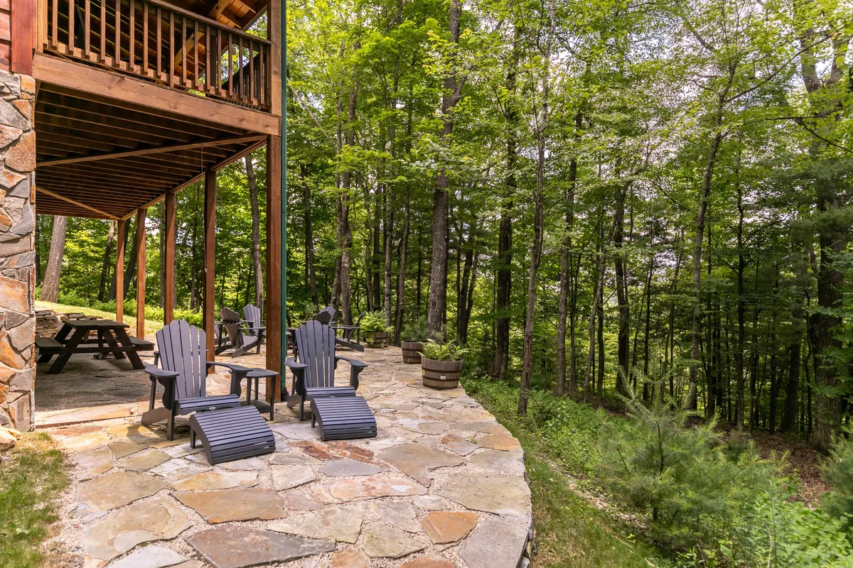 A natural stone patio with wooden chairs, nestled among mature trees, creating a tranquil and private outdoor setting ideal for enjoying mountain air and sunsets.