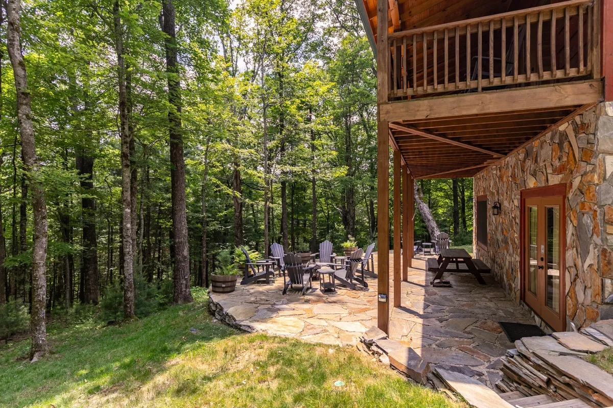 An inviting stone patio and wooden deck with outdoor seating is surrounded by trees. The area is perfect for outdoor dining, breathing in fresh mountain air, or firing up the grill for an al fresco dinner under the stars.